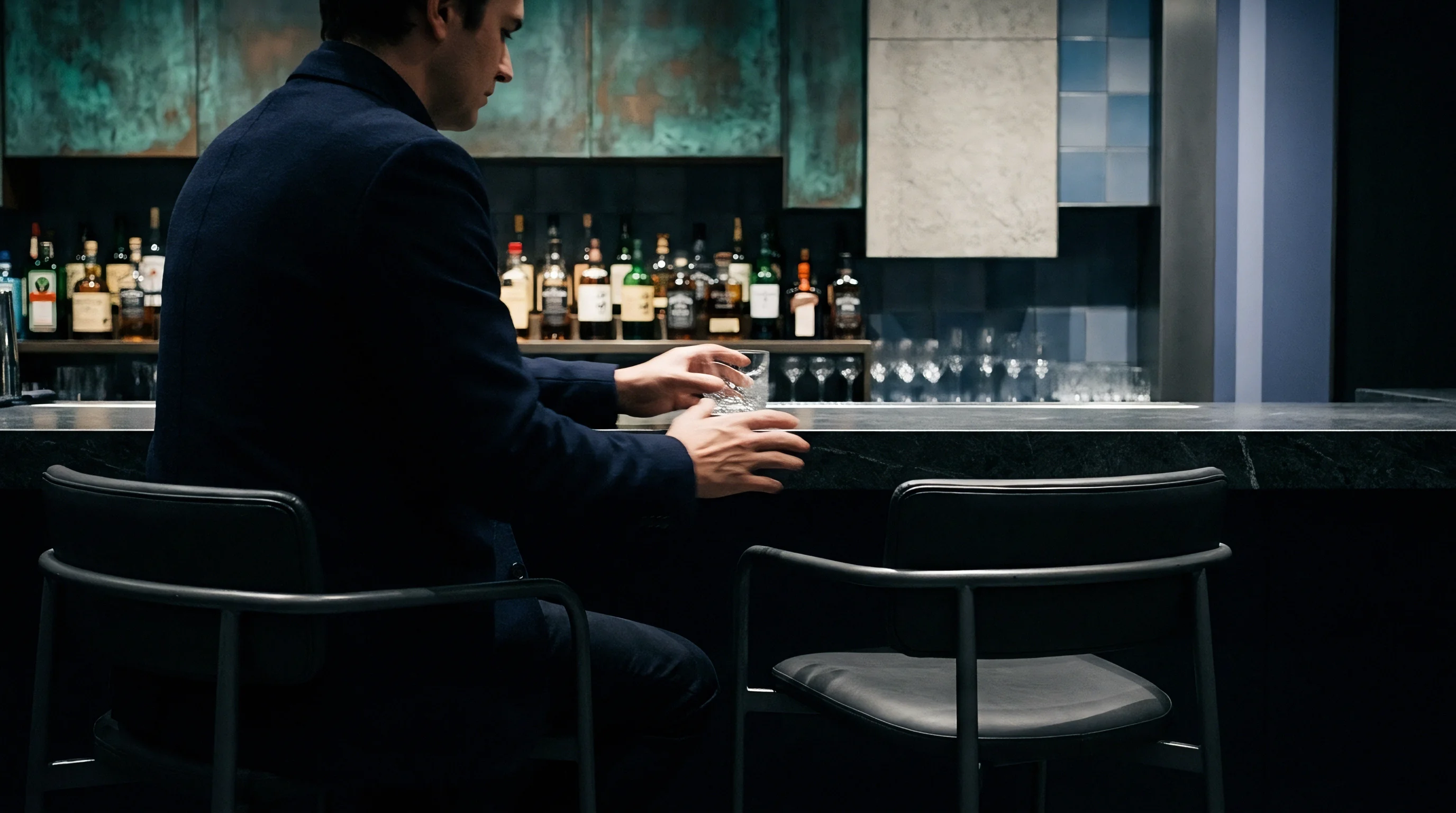 An industrial executive sits before a dark stone counter holding a crystal tumbler within a dim corporate lounge.