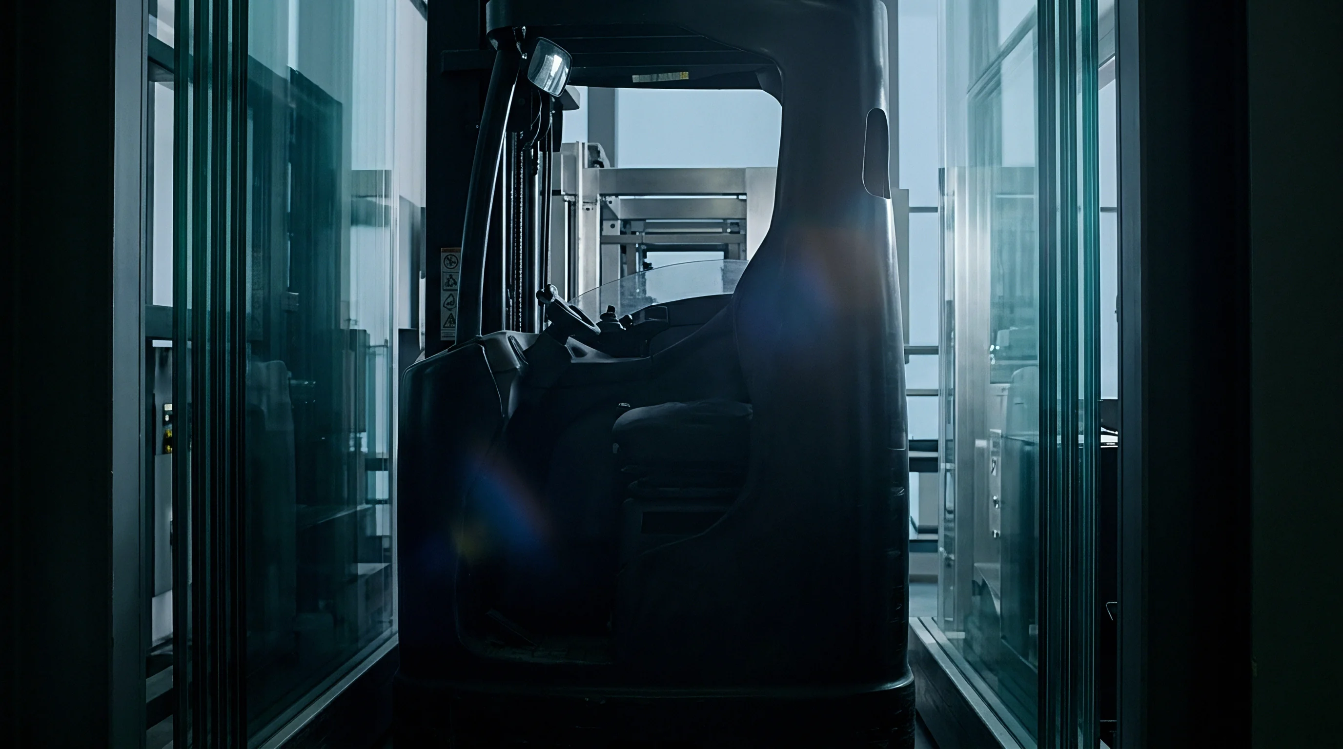 An industrial forklift sits stationary inside a glass enclosed corridor within a high density facility designed for automated production and material logistics.