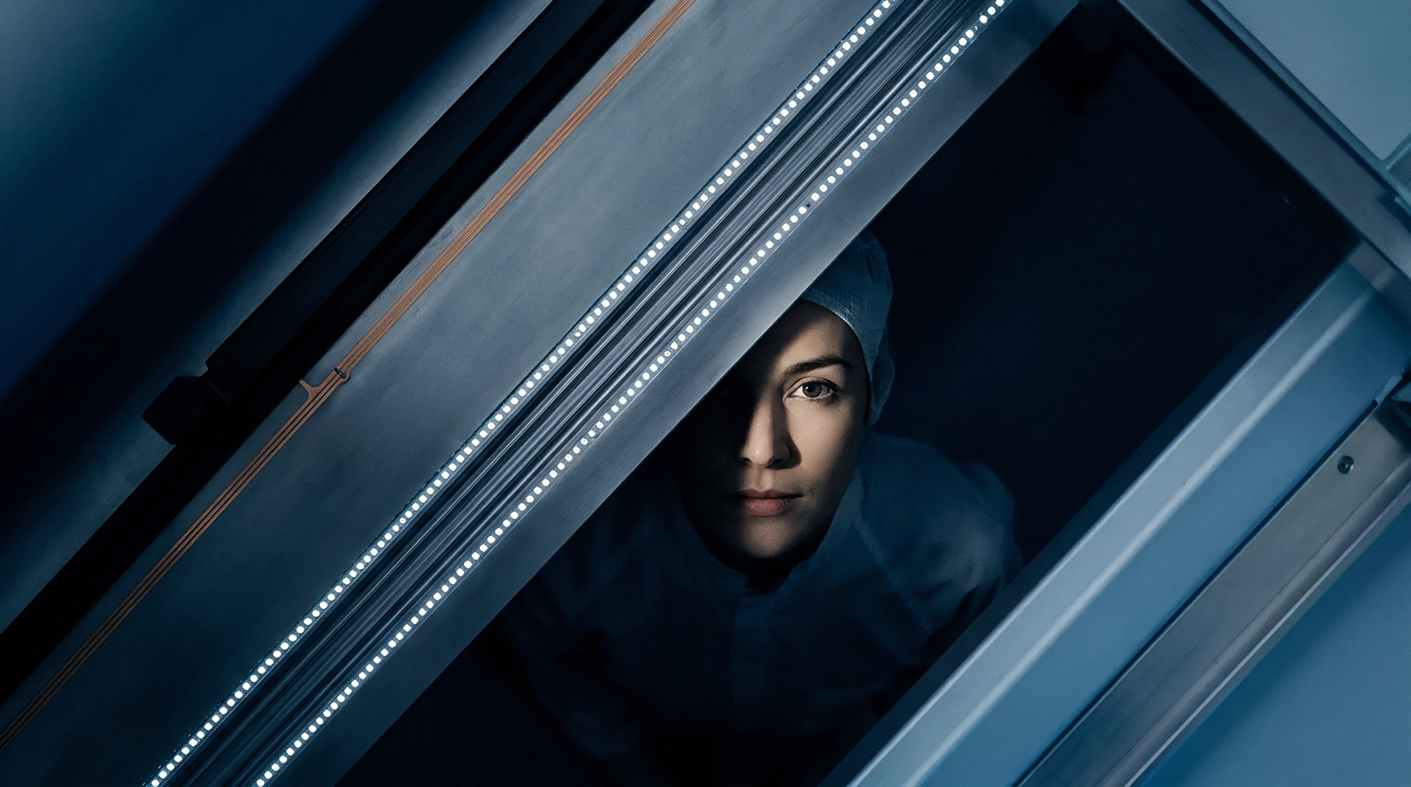 A technician in protective attire peers through the illuminated access hatch of heavy manufacturing machinery within a sterile facility.